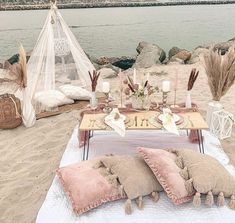 a table set up on the beach with pillows and blankets for two people to enjoy