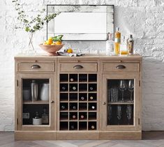 a wooden cabinet with wine bottles and glasses on it in front of a white brick wall