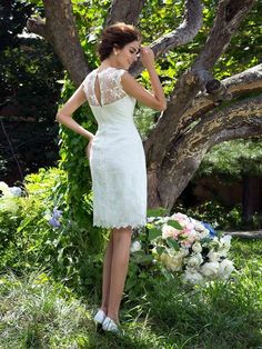 a woman standing in front of a tree wearing a dress with lace on the back