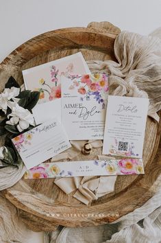 the wedding stationery is laid out on a wooden tray with flowers and greenery