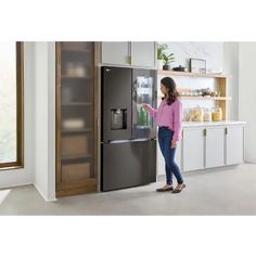 a woman is standing in front of the refrigerator and opening it up with her hand