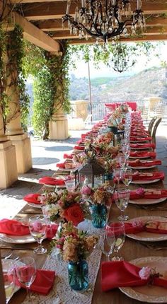 a long table is set with red napkins and place settings for an outdoor dinner