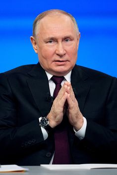 a man in a suit and tie sitting at a table with his hands folded up