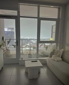 a living room with white furniture and large windows overlooking the cityscape in the distance