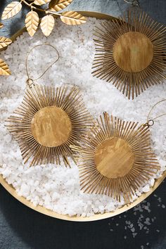 three gold sunburst earrings sitting on top of white rice