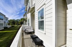 two chairs sitting on the front porch of a white house with blue sky in the background