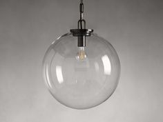 a clear glass globe light hanging from a black metal chain on a gray wall background