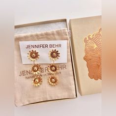 a pair of earrings in a box on top of a cloth bag with the packaging