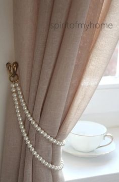 a curtain with pearls hanging on it next to a cup and saucer in front of a window