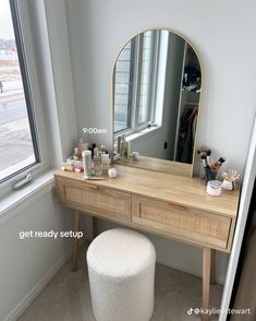 a vanity table with a mirror, stool and other items on it in front of a window