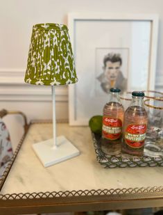 a table topped with two bottles of alcohol next to a lamp and framed photograph on the wall