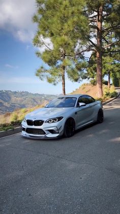 a silver car parked on the side of a road next to some trees and mountains