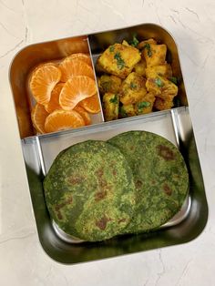 two trays filled with food on top of a white countertop next to orange slices