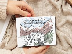 someone holding up a card that says you are my favorite adventure with mountains in the background