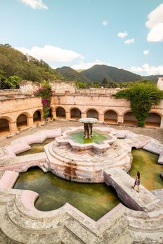 a person standing in the middle of a courtyard with a fountain and stone arches around it