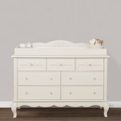 a white dresser with drawers and a baby crib in front of a gray wall