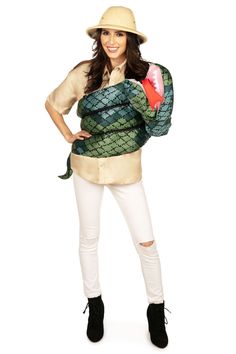 a woman in white pants and a hat is holding a green snake costume while posing for the camera