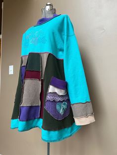 a blue and green jacket with patches on the front is hanging up against a wall