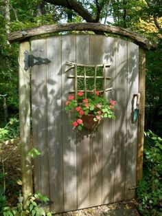 a small wooden outhouse with flowers in the pot on the door and an umbrella hanging from it's side