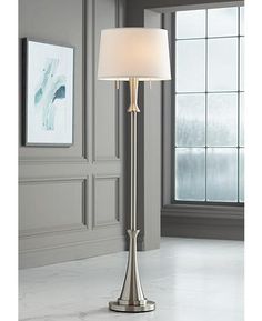 a floor lamp with a white shade on it in front of a wall and window