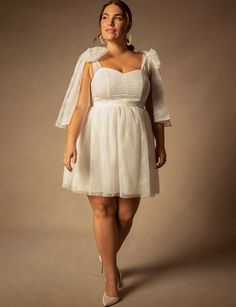 a woman in a short white dress with a veil on her head is posing for the camera