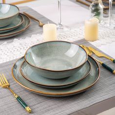 a place setting with plates and silverware on a table cloth, next to candles