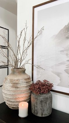 two vases sitting on top of a wooden table next to a candle and painting