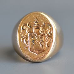 "A truly handsome vintage unisex armorial crest signet ring in solid 14k gold. this wonderful and weighty vintage signet ring features a hand engraved armorial crest on the oval front depicting a a sword topped knights helmet above a plaque with three stars and two dragons with flames in between them above water with a single fish and the Latin saying \"NEC ASPERA TERRENT\" in reverse below (meaning - They are not afraid of difficulties, or less literally \"Difficulties be damned.\" Motto for 27 Luxury Vintage Signet Ring With Center Stone, Luxury Vintage Signet Ring, Luxury Vintage Signet Ring With Maker's Mark, Luxury Vintage Signet Ring With Hallmarks, Classic 14k Gold Signet Ring For Ceremonial Occasions, Classic Collectible Signet Ring With Engraving, Classic Collectible Signet Ring With Coat Of Arms, Formal Gold Signet Ring With Coat Of Arms, Luxury Yellow Gold Coat Of Arms Signet Ring