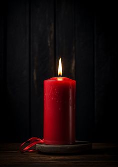 a red candle sitting on top of a wooden table next to a red ribbon and a black background