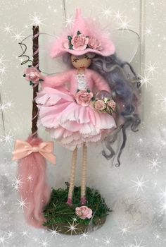 a doll is dressed in pink and holding a stick with flowers on it's head