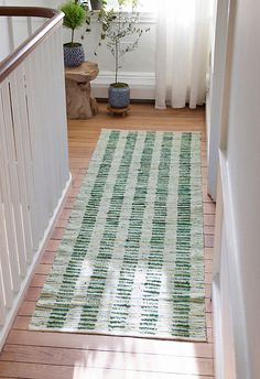 a green and white striped rug on the floor in front of a window with sunlight coming through it