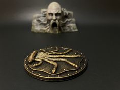 a bronze plate with a spider on it next to a figurine that looks like a human head