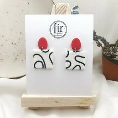 a pair of red and white earrings sitting on top of a wooden stand next to a potted plant