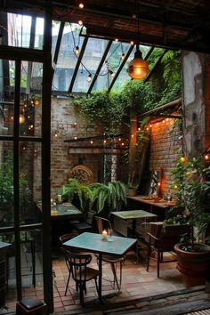 an outdoor patio with tables, chairs and potted plants on the walls is lit by hanging lights