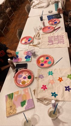 people sitting at a long table with paper plates and paintbrushes on the tables