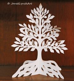 a white paper cutout of a tree on a wooden table with leaves and roots