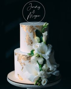 a white and gold wedding cake with flowers on the bottom tier is featured against a black background