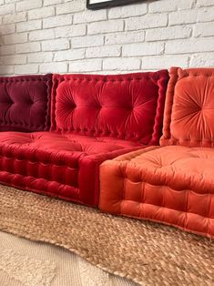 an orange and red couch sitting in front of a white brick wall on the floor