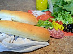 two sub sandwiches sitting on top of a table next to salads and condiments