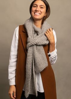 a woman wearing a brown vest and scarf smiles at the camera while standing in front of a gray background