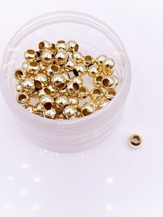 a plastic container filled with lots of gold colored beads on top of a white table