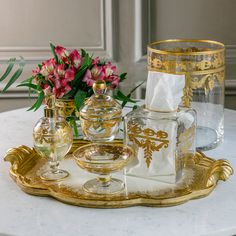 a tray that has some glassware on it and flowers in the vase behind it