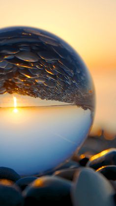 a glass ball sitting on top of rocks with the sun setting in the distance behind it