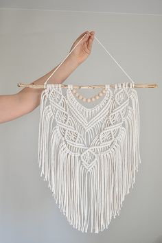 a person holding up a white macrame dream catcher