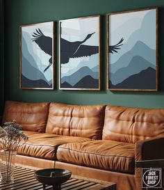 two paintings hang on the wall above a leather couch in a living room with green walls