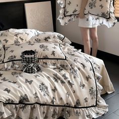 a woman standing in front of a bed with white sheets and black butterflies on it