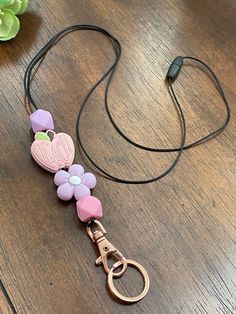 a lanyard with flowers and a heart on it sitting on a wooden table next to a pair of headphones