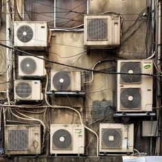 many air conditioners are attached to the side of a building with wires running through it