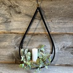 a candle hanging from a wall with greenery around it and a black leather cord