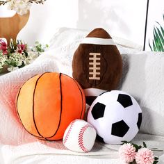 three stuffed sports balls sitting on top of a bed next to a vase with flowers